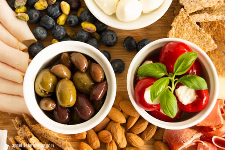 Mixed olives on an antipasto board with blueberries, almonds, mozzarella balls and piquante peppers - 5 Tips For Busting Your Carb Cravings On Keto